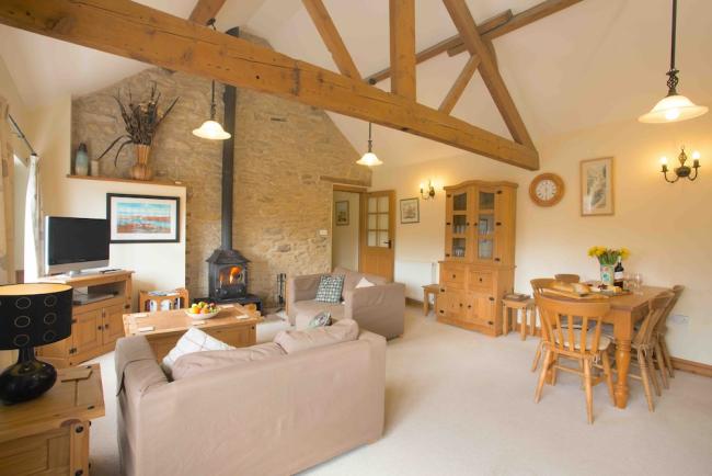 A spacious, oak-beamed lounge area with sofas, TV, wood burner and dining table.
