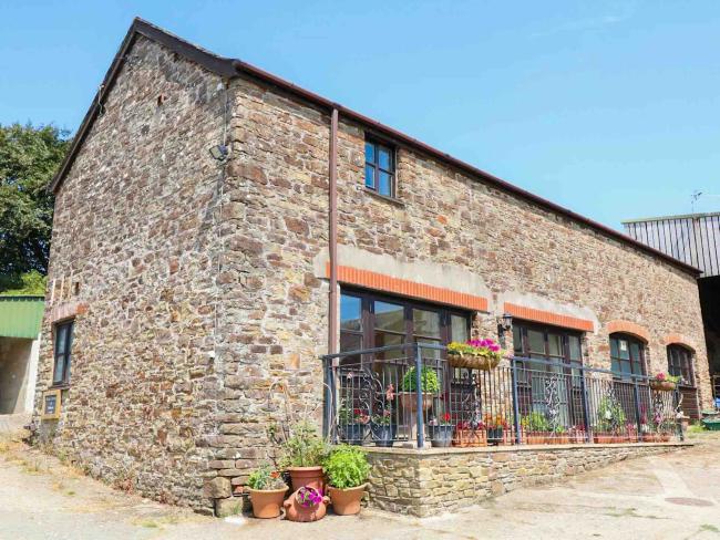 Exterior of a stone-built barn conversion in Bideford with large floor-to-ceiling windows on the ground floor overlooking a courtyard with flower pots lining the wall.