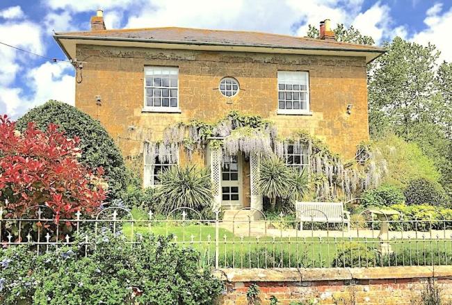 Exterior of a wisteria-clad, double-fronted Georgian House and front garden.