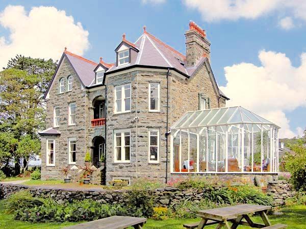 £-storey Stone house and conservatory surrounded by gardens.