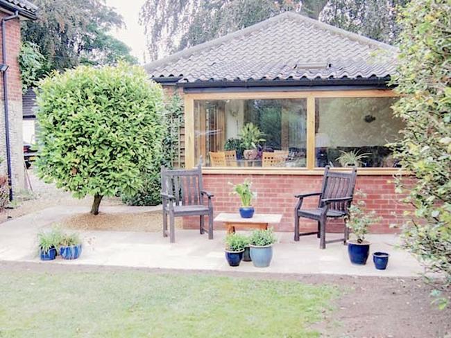 Exterior of a single storey Norfolk holiday lodge With a patio and lawn.