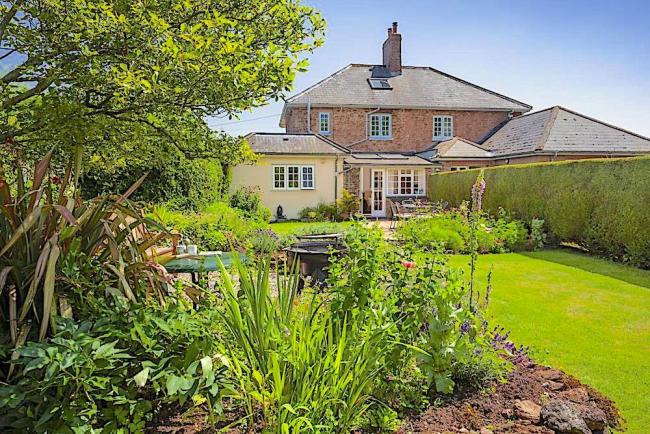 A brick house overlooks a large lawn with flower-filled borders