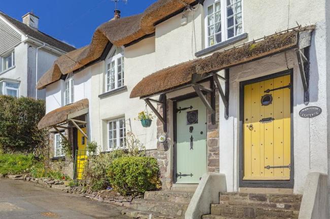 The exterior of a small terrace of thatched cottages overlooks a quiet North Devon village street.