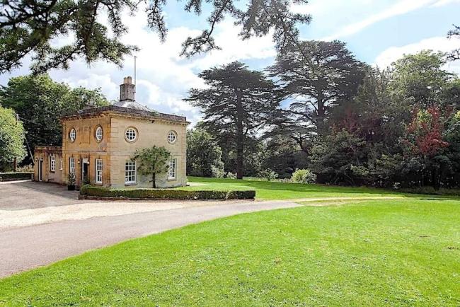 Exterior of a stone-built Cotswold country house surrounded by trees and parkland.