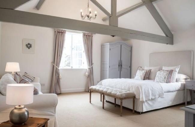 A spacious oak-beamed double bedroom with a bed, wardrobe and large sofa.