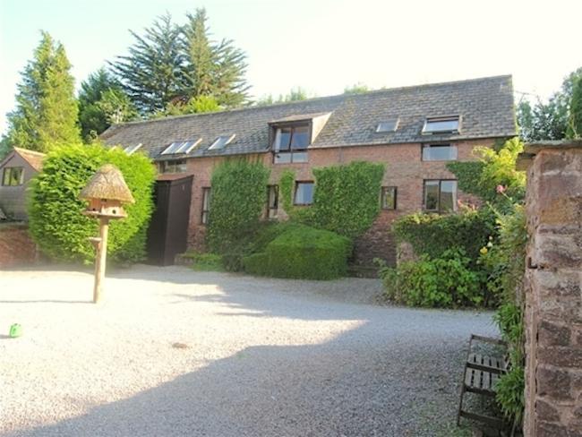 Exterior of a 2-storey Somerset barn conversion overlookig a large courtyard with trees on its edges.