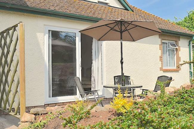 The exterior of a chalet bungalow with a courtyard containing a table with a parasol and chairs.