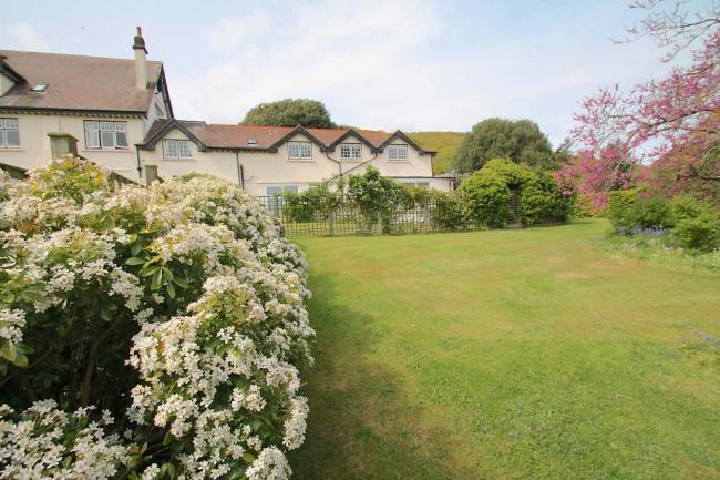 A large Someerset house overlooks a spacious lawn lined by flowering shrubs and trees.