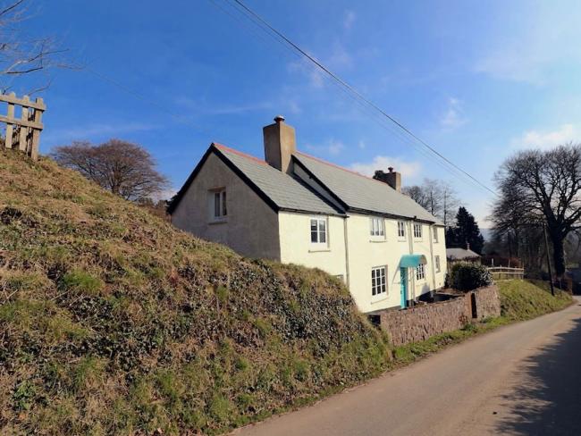 An Exmoor Longhouse overlooks a quiet, steep-banked country lane.