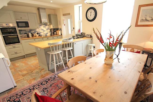 A fitted kitchen with breakfast bar and a pine-wood dining table seating 6.