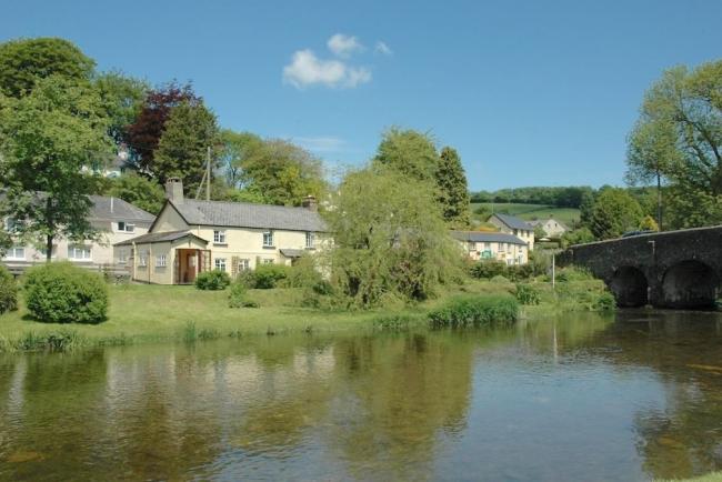 An Exmoor holiday home on the banks of the calm River Barle flowing under a stone bridge.