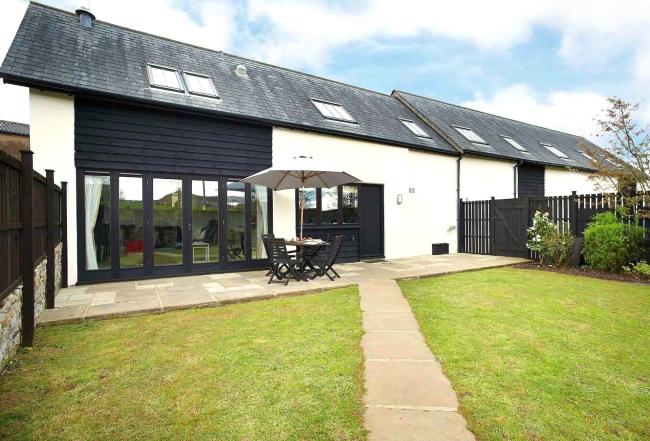 A semi-detached, part-timbered contemporary cottage with bi-fold windows, patio and a spacious lawn.
