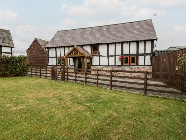A historic 'black-white white' timbered Herefordshire farm cottage sits behind a terraced and fenced-in lawn.