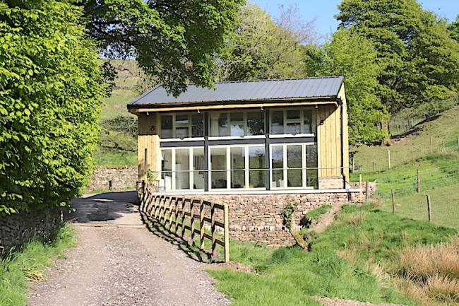 Exterior of a contemporary country cottage with a full-width balcony and floor-to-ceiling bi-fold glass doors.