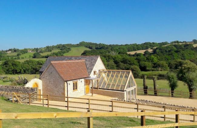 A stone-built cottage with a large glass roofed sun room overlooking fields and a wooded valley.