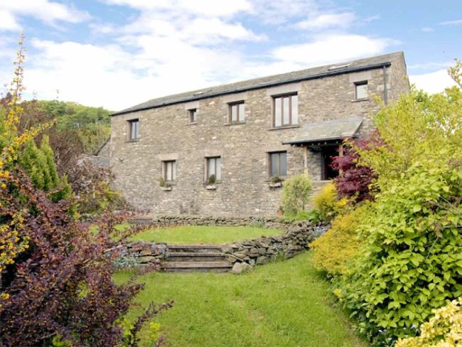 A barn conversion in Kendal overlooks a lawn surrounded by mature shrubs and bushes.