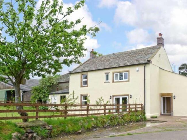 A wood and slate Cotswold holiday cottage overlooks a terrace with a dining table and lawn.