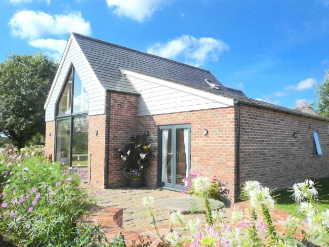 The exterior of a modern Suffolk holiday home with large windows on both floors overlooking a flower-filled garden.