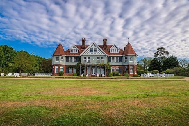 A grand Victorian Manor House with two turreted wings overlooks a large lawn.