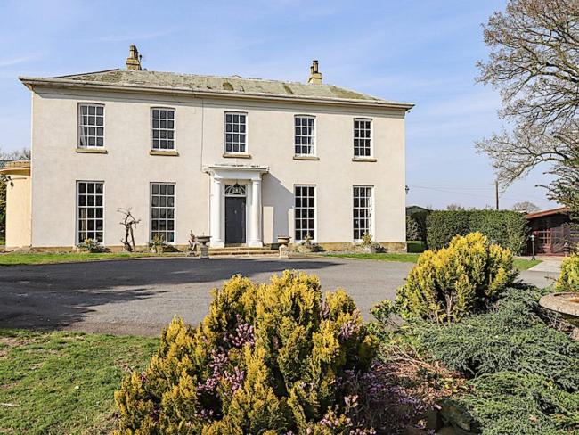 A classic country house with a pillared front entrance and surrounded by lawns and mature flower beds