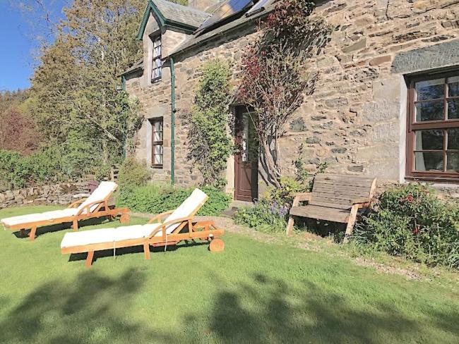 Sun loungers on a lawn in front of a stone-built holiday cottage
