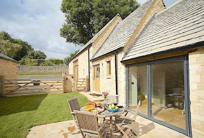 A side elevation of a luxury Cotswold Barn conversion with wide, full-height sliding French Windows.