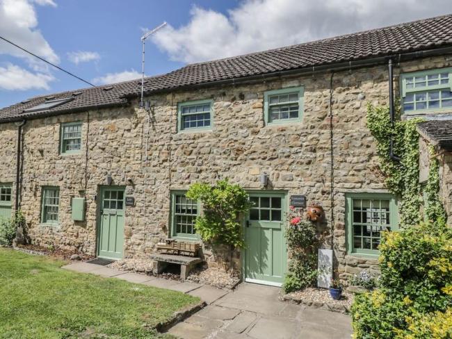 A terrace of 3-stone-built Bedale holiday cottages facing a lawn.