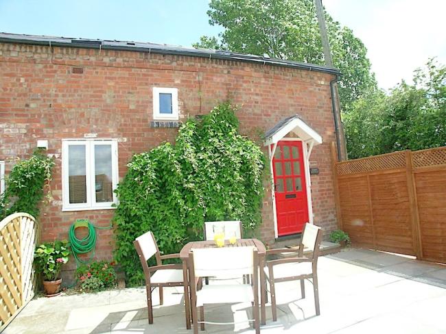 Exterior of a creeper-clad brick cottage with an outdoor table and chairs on a paved courtyard.