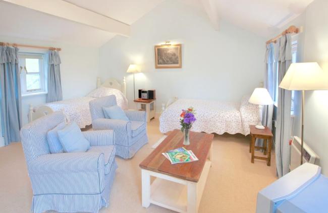 A tall stone barn conversion and annexe surrounded by a lawn, open fields and mature woods.