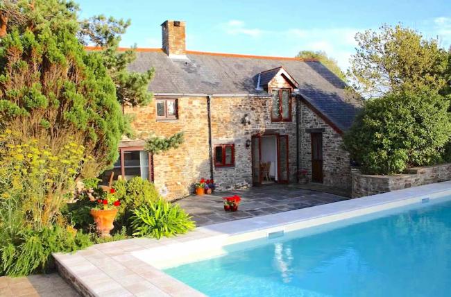 An outdoor swimming pool overlooked by a stone-built holiday cottage in North Devon