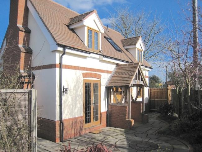 A double fronted modern chalet bungalow with a terraced garden behind a fence.