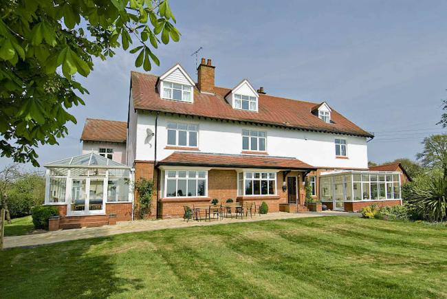 Exterior of a large country house with a conservatory and large lawn.