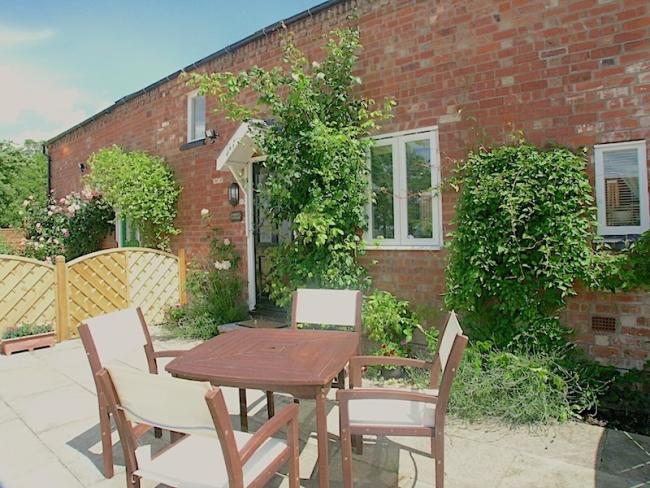The exterior of a rural holiday cottage has a courtyard garden and a dining table with chairs.
