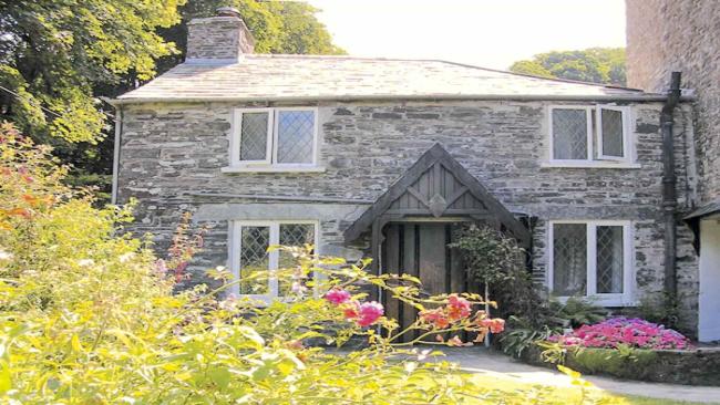 A double-fronted stone cottage overlooks a sunny lawn edged with flowers.