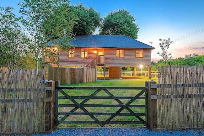A timber house on stilts beneath lime trees overlooks a large fenced garden.