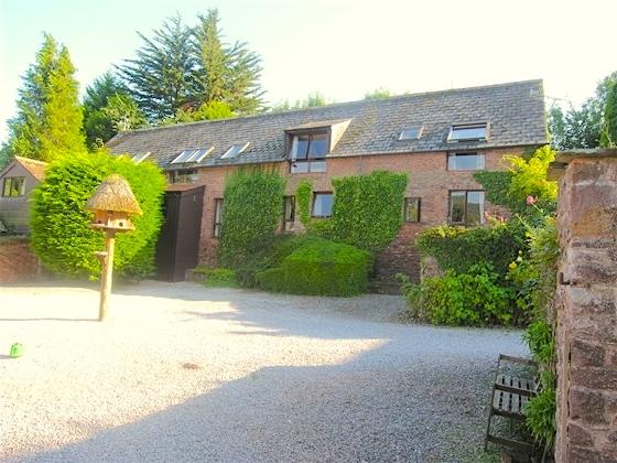 The exterior of a rural holiday cottage in Somerset is ivy-clad and overlooks a small front garden and a spacious courtyard.