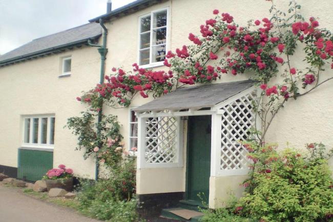 Climbing roses surround the porch of a country cottage in Somerset.