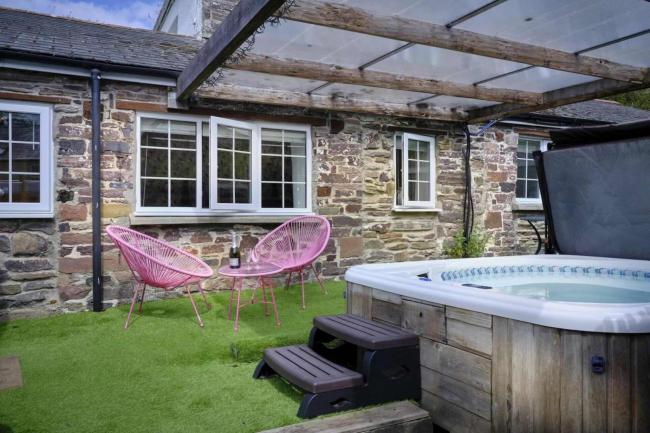 A stone built Exmoor cottage  faces a lawn containing a sheltered hot tub  and a two outdoor chairs around a tea-table.