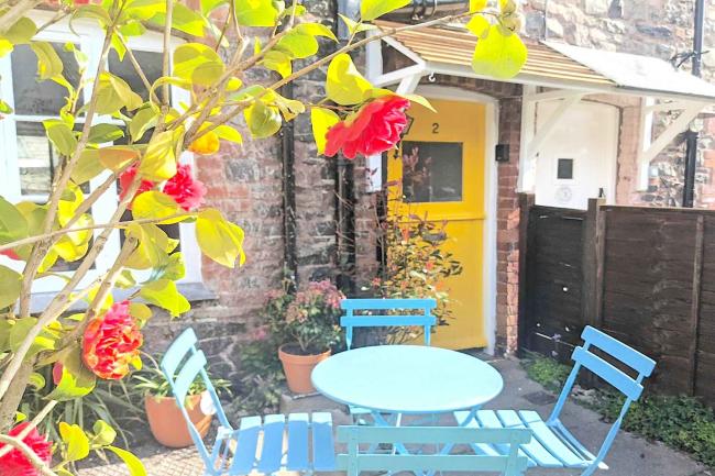 A leafy courtyard with a table and chairs in front of a stone-built Somerset coastal cottage.