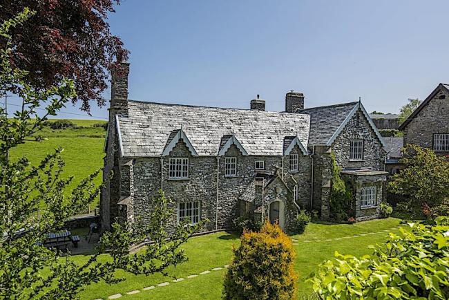 A large stone-built Exmoor cottage surrounded by trees and open fields.
