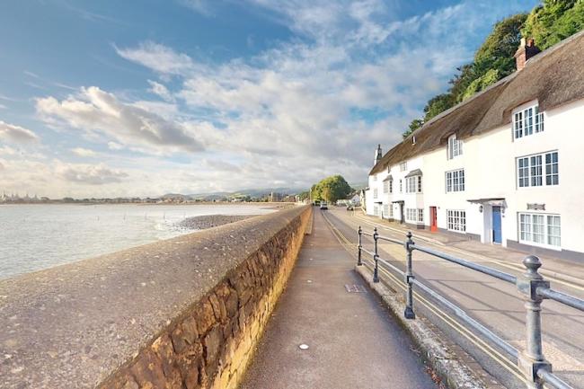 A terrace of thatched cottages overlooks a road and beachfront at low tide.