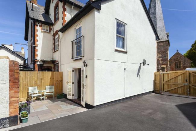 Exterior of a 2-storey cottage with courtyard and large tarmac parking space.