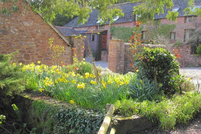 Exterior of a stone-built holiday home in Dunster surrounded by a stone wall..