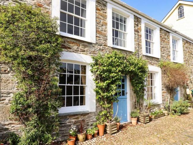 Exterior of a wisteria-clad, terraced holiday cottage in Mevagissey overlooking a cobbled street.