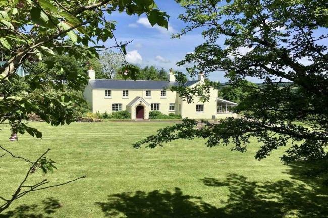 An Exmoor farmhouse overlooks a large lawn surrounded by trees.
