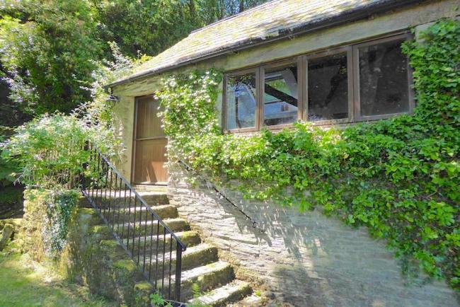 The leafy-clad exterior of a stone-built single-storey Exmoor holiday cottage with a flight of stone steps to the front door.