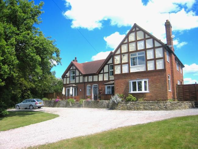 A modern cross-timbered gable overlooking a drive, lawn and a spacious parking area.