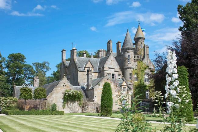 A multi-turreted Scottish castle in landscaped gardens.