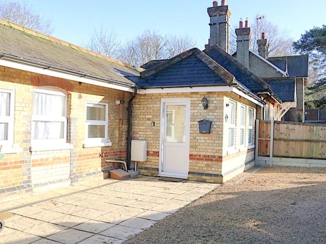 Exterior of a1930s brick built bungalow with a patio and shingled secure parking area.