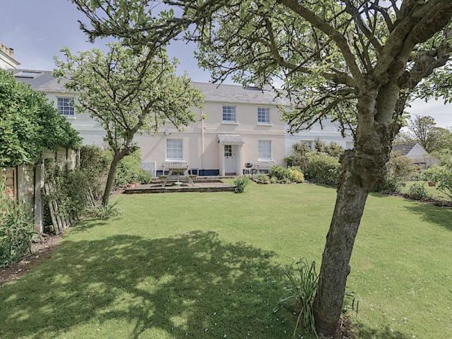 A double-fronted Hope Cove holiday cottage overlooks a large lawn.